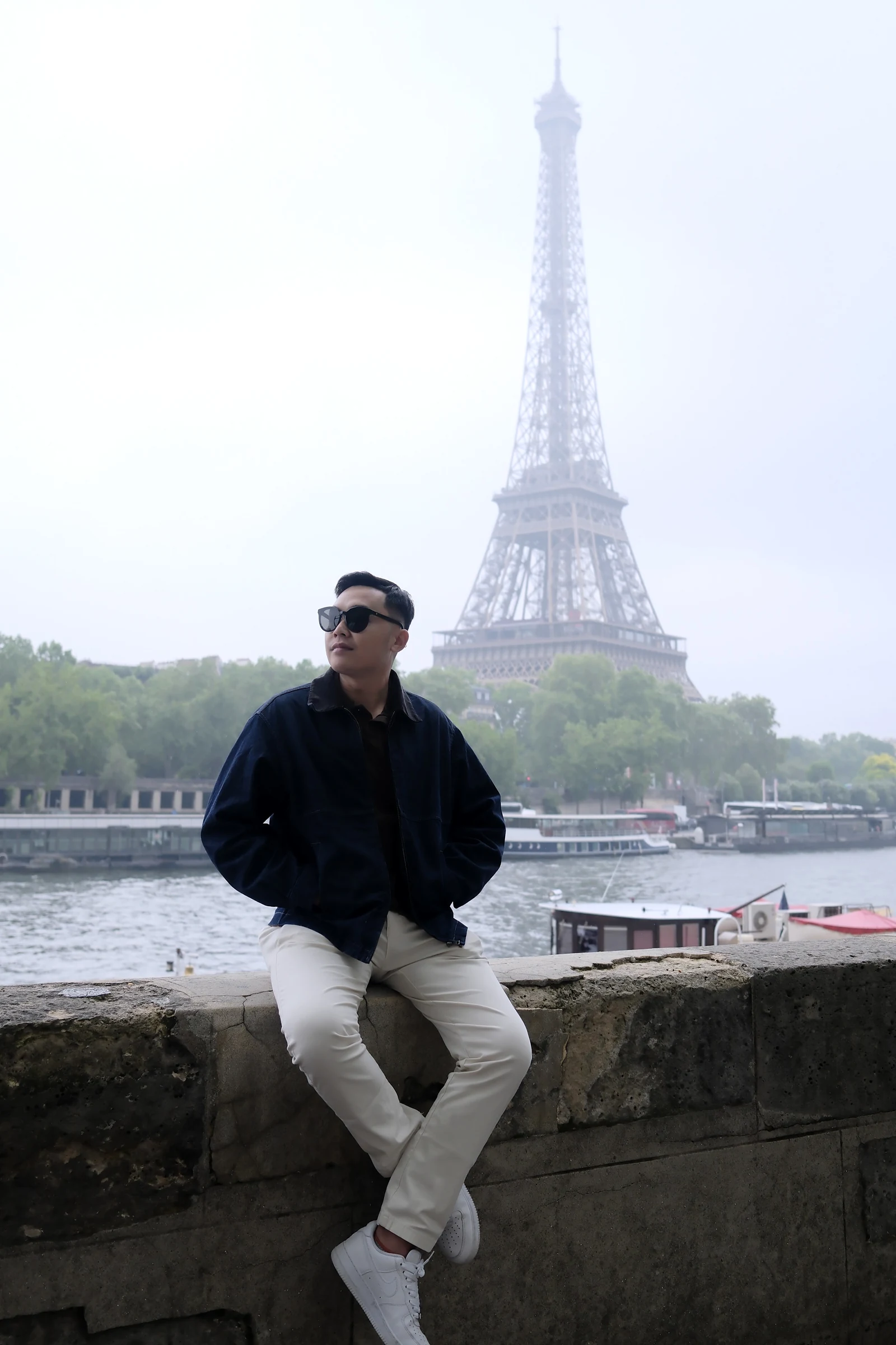 Nguyễn Bá Lục ngồi bên sông, phía xa là tháp Eiffel